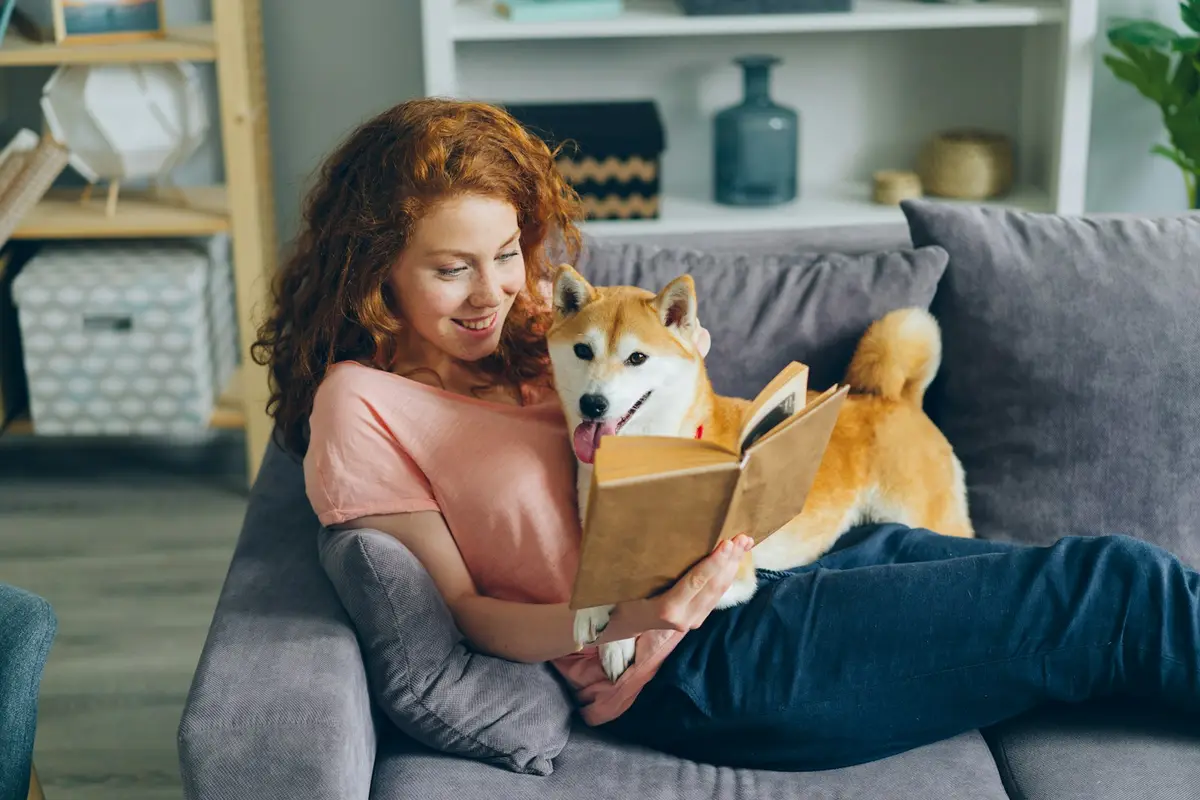 A woman reading on the sofa while caring for her dog